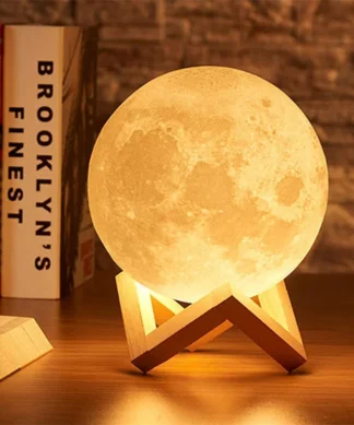 A moon-shaped lamp on a wooden stand, glowing warmly on a wooden table, with books and a brick wall in the background. | 28Alchemy