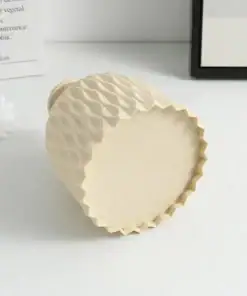 A textured beige ceramic vase lying on its side on a white surface, near a single white flower and paper in the background. | 28Alchemy