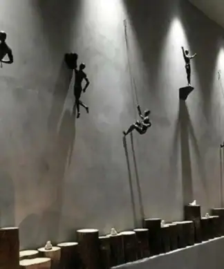Wall art of four metal figures climbing ropes, mounted above wooden blocks under dramatic lighting, casting shadows. | 28Alchemy
