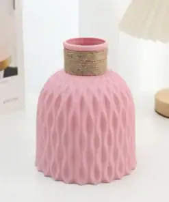 Pink textured vase with a twine-wrapped neck placed on a light surface near a wooden lamp and a book. | 28Alchemy