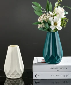White and teal geometric vases on a glossy surface. The teal vase holds white and green flowers. Books are placed underneath. | 28Alchemy