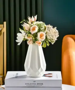 White vase with pink and white flowers on a stack of books, near an orange chair and gold shelf, against a dark green wall. | 28Alchemy
