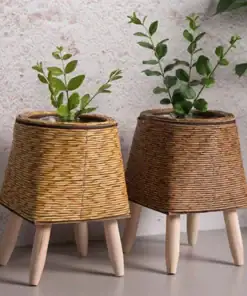 Two Rattan Planter Stands with wooden legs, each holding a small plant, on a light gray surface. | 28Alchemy