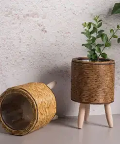 Two Rattan Planter Stands: one upright with a plant and wooden legs, the other tipped over, against a textured wall. | 28Alchemy