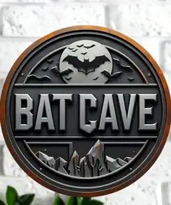 Round sign with “BAT CAVE” text, mountains, bats, and a large bat symbol, mounted on a white brick wall. | 28Alchemy