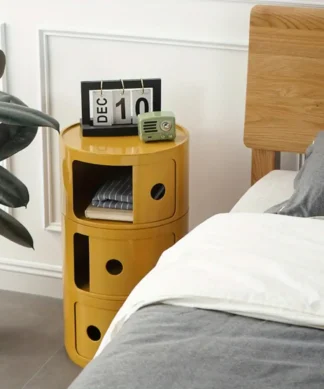 Yellow round nightstand with three compartments, a calendar, and radio beside a bed with gray and white bedding. | 28Alchemy