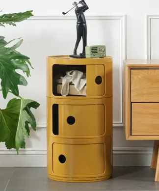Yellow round storage cabinet with three compartments beside a wooden dresser, topped with decor items and a plant nearby. | 28Alchemy