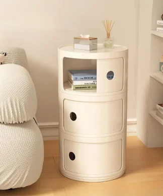 Cream-colored round nightstand with books and decor beside a textured white sofa on a wooden floor. | 28Alchemy