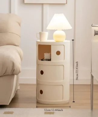 A round, cream-colored side table with three compartments, lamp, mug, and book next to a beige sofa; dimensions shown. | 28Alchemy