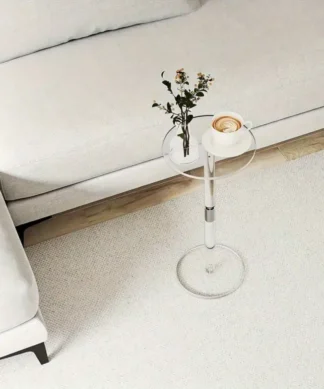 A small glass side table with a vase of flowers and a pastry sits by a white couch on a light carpeted floor. | 28Alchemy