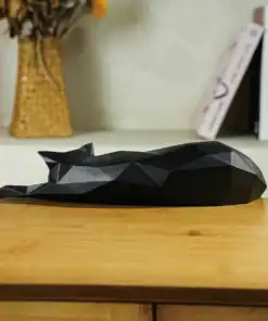 Geometric black cat sculpture lying down on a wooden table, with books and a vase in the background. | 28Alchemy
