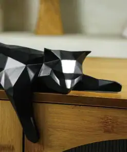 A black geometric cat sculpture lies on its side across the edge of a wooden table. | 28Alchemy