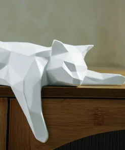 White geometric cat sculpture lying stretched out on a wooden surface, with one paw hanging over the edge. | 28Alchemy