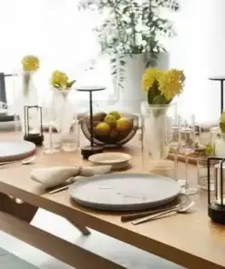 A wooden dining table set with plates, napkins, glasses, candles, and yellow flowers in vases. | 28Alchemy