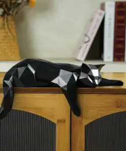 A geometric black cat sculpture lies stretched out on top of a wooden cabinet with books and a vase in the background. | 28Alchemy