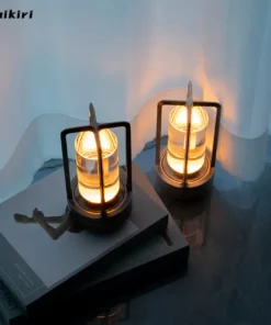 Two modern lantern-style lights on a blue floor, one sits on a closed book, both glowing warmly near a white curtain. | 28Alchemy