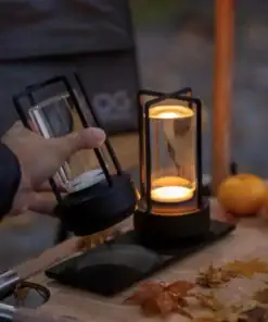 A hand lifts a portable lantern next to another lit lantern on a table with autumn leaves and oranges. | 28Alchemy