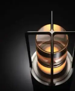 A modern, cylindrical lamp with a warm glow, surrounded by metal bars, sits on a dark, reflective surface. | 28Alchemy