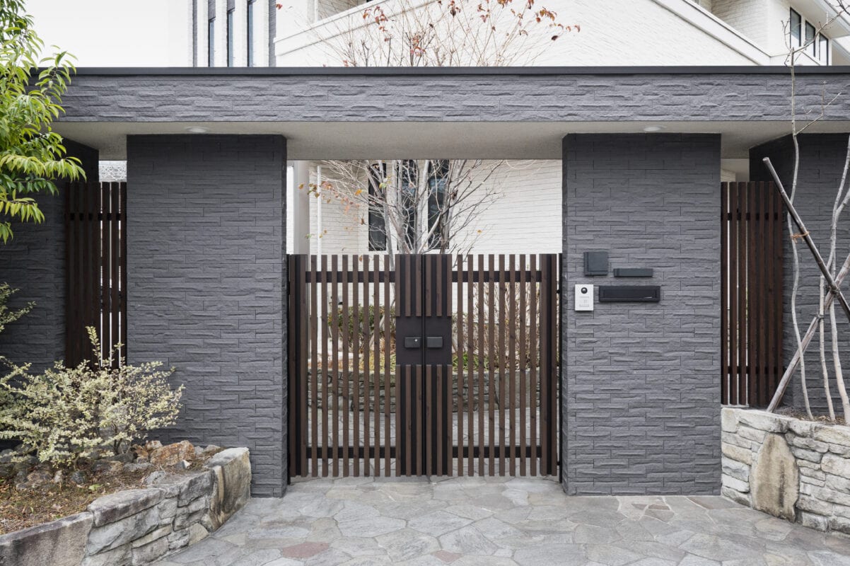 Modern gray stone gate with wooden slats, mailboxes, and intercom at the entrance of a house with plants nearby. | 28Alchemy