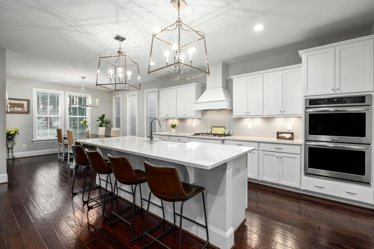 Modern kitchen with white cabinets, an island with brown barstools, pendant lights, and stainless steel appliances. | 28Alchemy