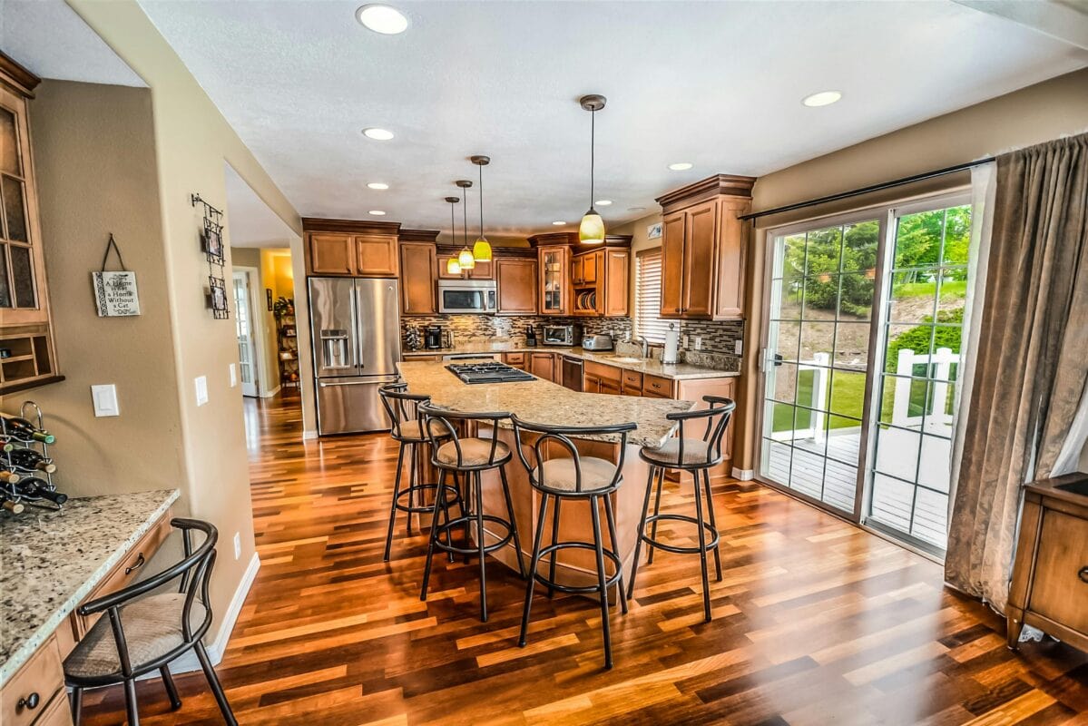 Modern kitchen with wooden cabinets, island seating, stainless steel appliances, and sliding glass doors to a deck. | 28Alchemy