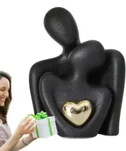 A smiling woman holding a gift next to a black abstract couple figurine with a golden heart. | 28Alchemy