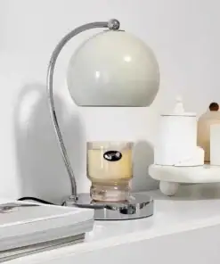 Modern white and chrome desk lamp beside a glass candle on a white shelf with minimal decor. | 28Alchemy