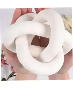 Two hands hold a smooth, white, sculptural knot with a soft, matte texture; pink flowers are nearby. | 28Alchemy