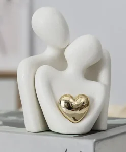 Minimalist white sculpture of two faceless figures embracing, with a gold heart in the center. | 28Alchemy