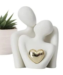 White abstract sculpture of two embracing figures with a gold heart, next to a small potted succulent plant. | 28Alchemy