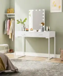White vanity table with mirror and lights, makeup items, and decor in a cozy, modern bedroom with clothes hanging nearby. | 28Alchemy