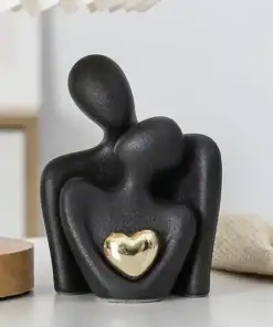 Abstract black sculpture of two figures embracing, one holding a shiny gold heart, on a white surface. | 28Alchemy