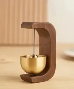 A small wooden and brass tabletop bell with a modern, minimalist design sits on a light wood surface. | 28Alchemy