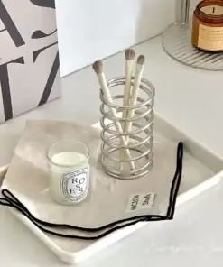 A tray holds a candle, a linen cloth, makeup brushes in a holder, and a lit candle in the background. | 28Alchemy
