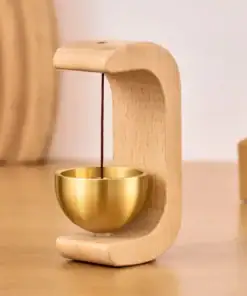 A small gold bowl suspended by string in a curved wooden stand on a wooden surface. | 28Alchemy