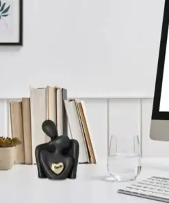 Black abstract sculpture with a gold heart on a white desk, near books, a plant, a glass of water, and a computer monitor. | 28Alchemy