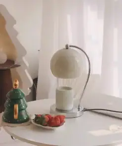 A white lamp, a green Christmas tree mug, strawberries, and a candle sit on a round white table by sheer curtains. | 28Alchemy