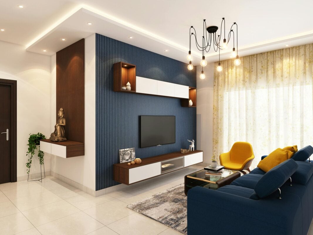 Modern living room with blue accent wall, TV, stylish house design, blue sofa, yellow chair, and sheer-curtained window. | 28Alchemy