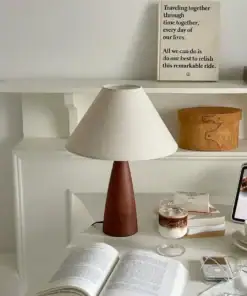 A cozy desk setup with a brown lamp, books, a drink, and a framed inspirational quote on a white shelf in the background. | 28Alchemy