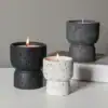 Three textured stone candles, two black and one white, with two lit and one unlit, on a white surface and book. | 28Alchemy