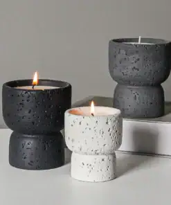 Three textured stone candles, two black and one white, with two lit and one unlit, on a white surface and book. | 28Alchemy