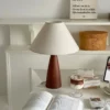 A cozy desk with a lamp, open book, coffee, and decorative items arranged neatly on white shelves. | 28Alchemy