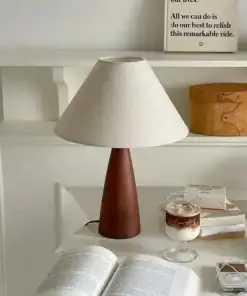 A cozy desk with a lamp, open book, coffee, and decorative items arranged neatly on white shelves. | 28Alchemy
