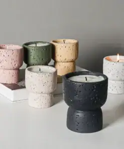Five textured candles in various colors sit on a white surface; one candle is lit, others are unlit. | 28Alchemy