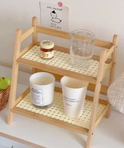 Two-tier wooden shelf holds a candle, a white cup, a glass, a small jar, and is beside a basket of green grapes. | 28Alchemy