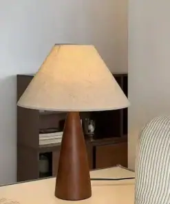 A wooden table lamp with a beige lampshade sits on a white desk beside a striped chair. | 28Alchemy