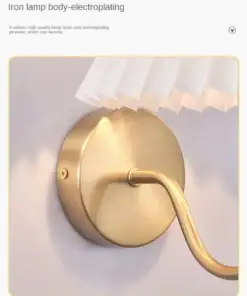 Close-up of a gold-colored, wall-mounted lamp with a round base and a pleated white lampshade. | 28Alchemy