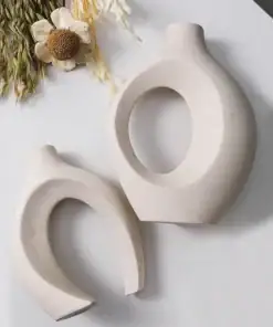 Two modern, beige ceramic vases with oval cutouts, next to dried wheat and a white flower on a light surface. | 28Alchemy
