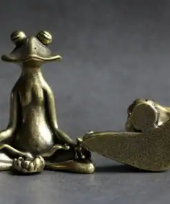 Bronze figurine of a meditating frog in a yoga pose next to a small reclining bird statue on a gray surface. | 28Alchemy