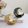 Gold and black crescent moon candle holders with lit candles on a table beside a book and a vase of flowers. | 28Alchemy